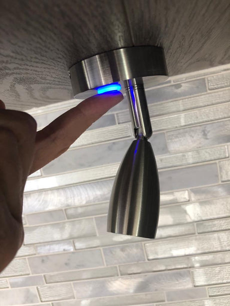 Finger activates a blue-lit touch control for an adjustable reading light, often found in an RV rental.