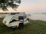 Misty sunrise scene: a white teardrop RV rental parked by foggy water, highlighting serene camping.