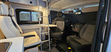 Spacious rv rental interior: view showing driver's cabin with dark seats, and light living area seats, table, and bunk ladder.