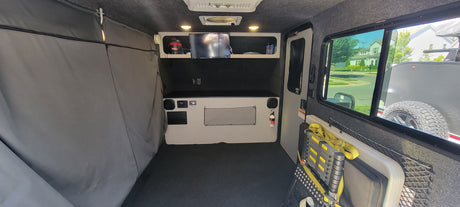 Interior of an RV rental: functional space with sleeping area, storage, small TV, controls, and window views. Perfect for travel.