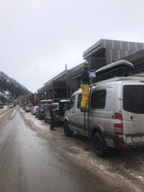 Man on an RV rental's ladder holds Drumsticks on a slushy street in a snowy mountain town.
