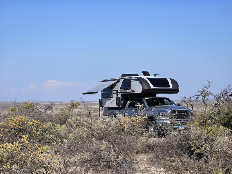This truck camper RV rental is set up in a remote, arid landscape under a clear blue sky, ideal for off-grid adventures. — photo 12