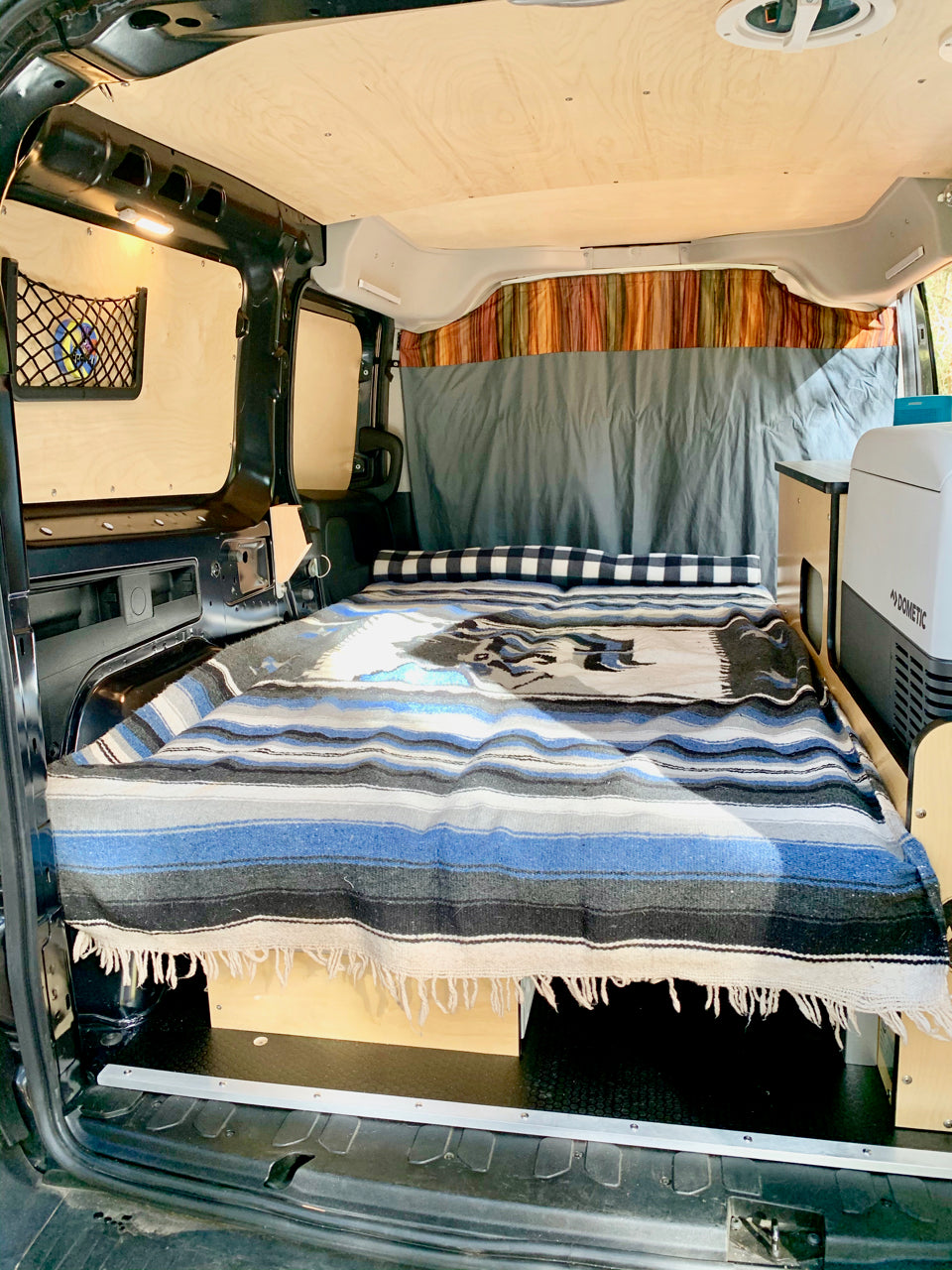 This RV rental's cozy camper van interior features a bed with storage, wood paneling, and a Dometic cooler.