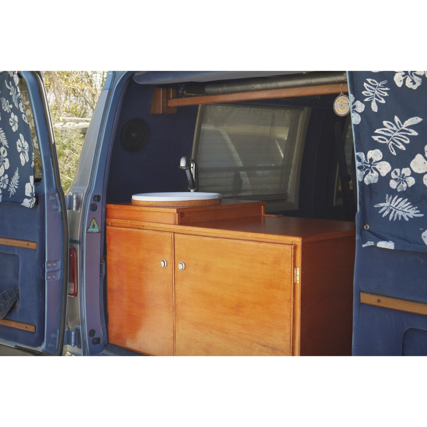 Explore this RV rental's custom van conversion: a cozy kitchen with wood cabinets, sink, and patterned blue curtains. — photo 5