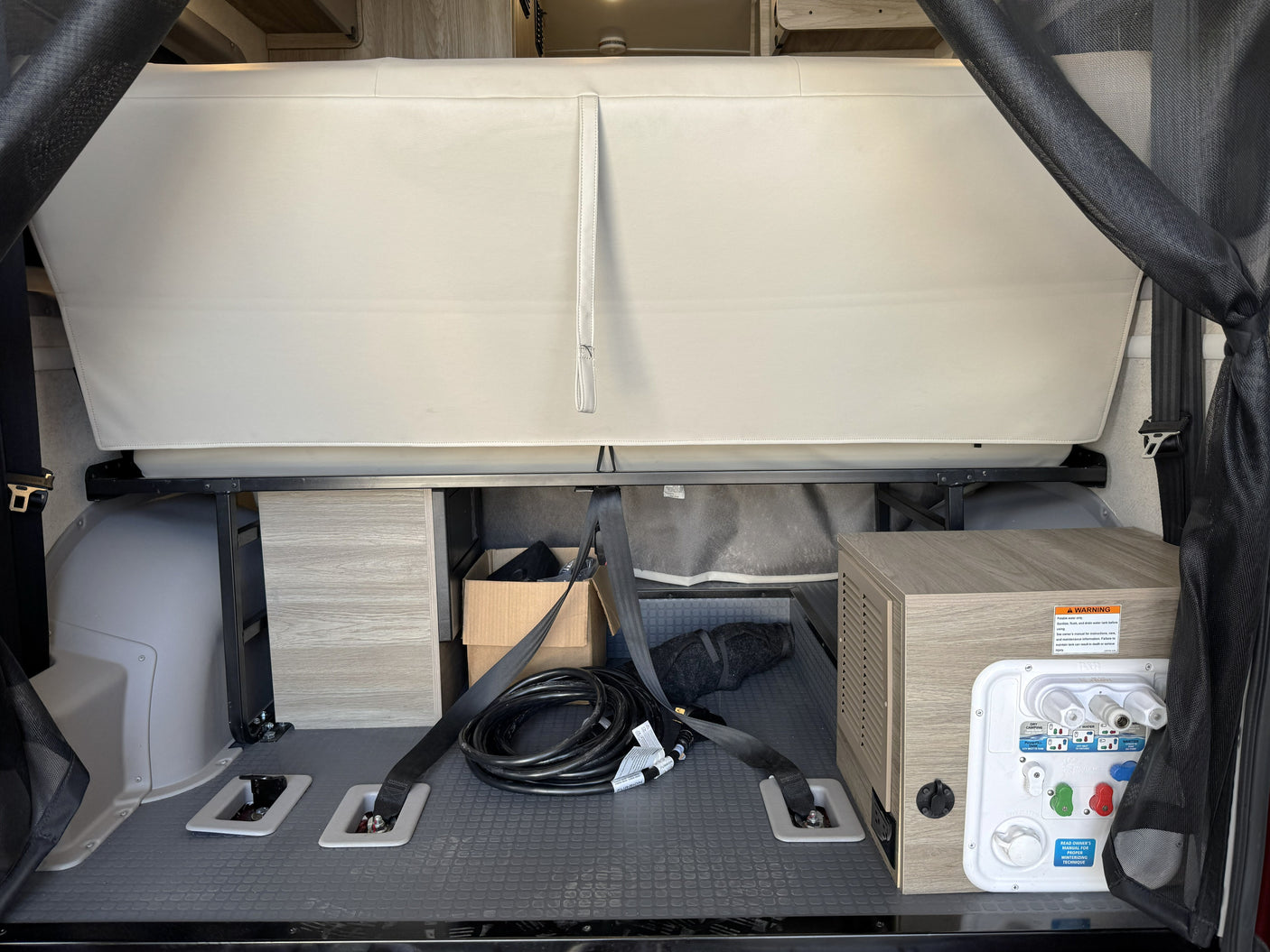 RV rental's rear cargo: Folded bed, organized power cable, and water utility panel (with warning) ensure readiness for adventure.
