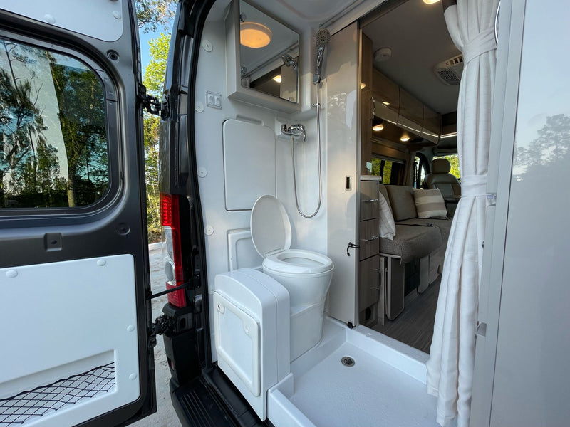 Compact **rv rental** interior: wet bath with toilet, shower, mirror, leading to the main living space. — photo 15
