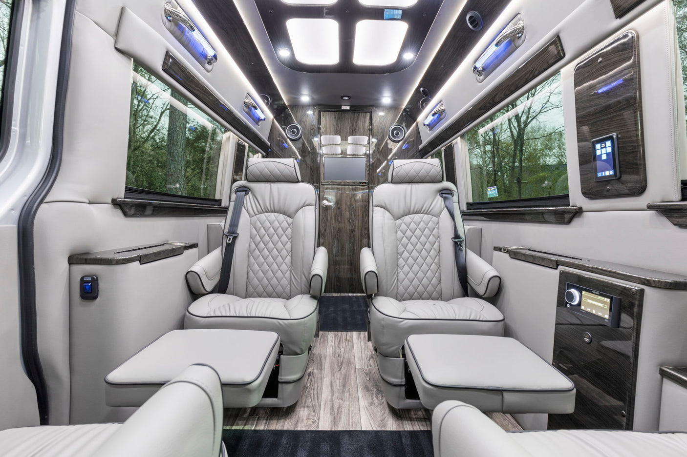 Plush grey captain's chairs with footrests in a luxurious RV rental van's interior, featuring wood flooring and ambient lighting.