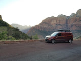 This rv rental camper van with a roof box enjoys a stunning mountain view at a national park, perfect for a scenic trip.