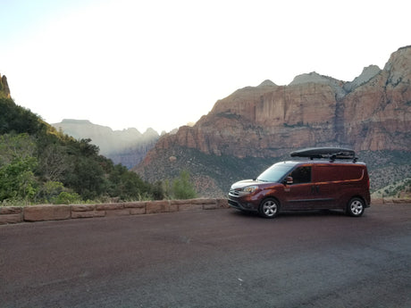 This rv rental camper van with a roof box enjoys a stunning mountain view at a national park, perfect for a scenic trip.