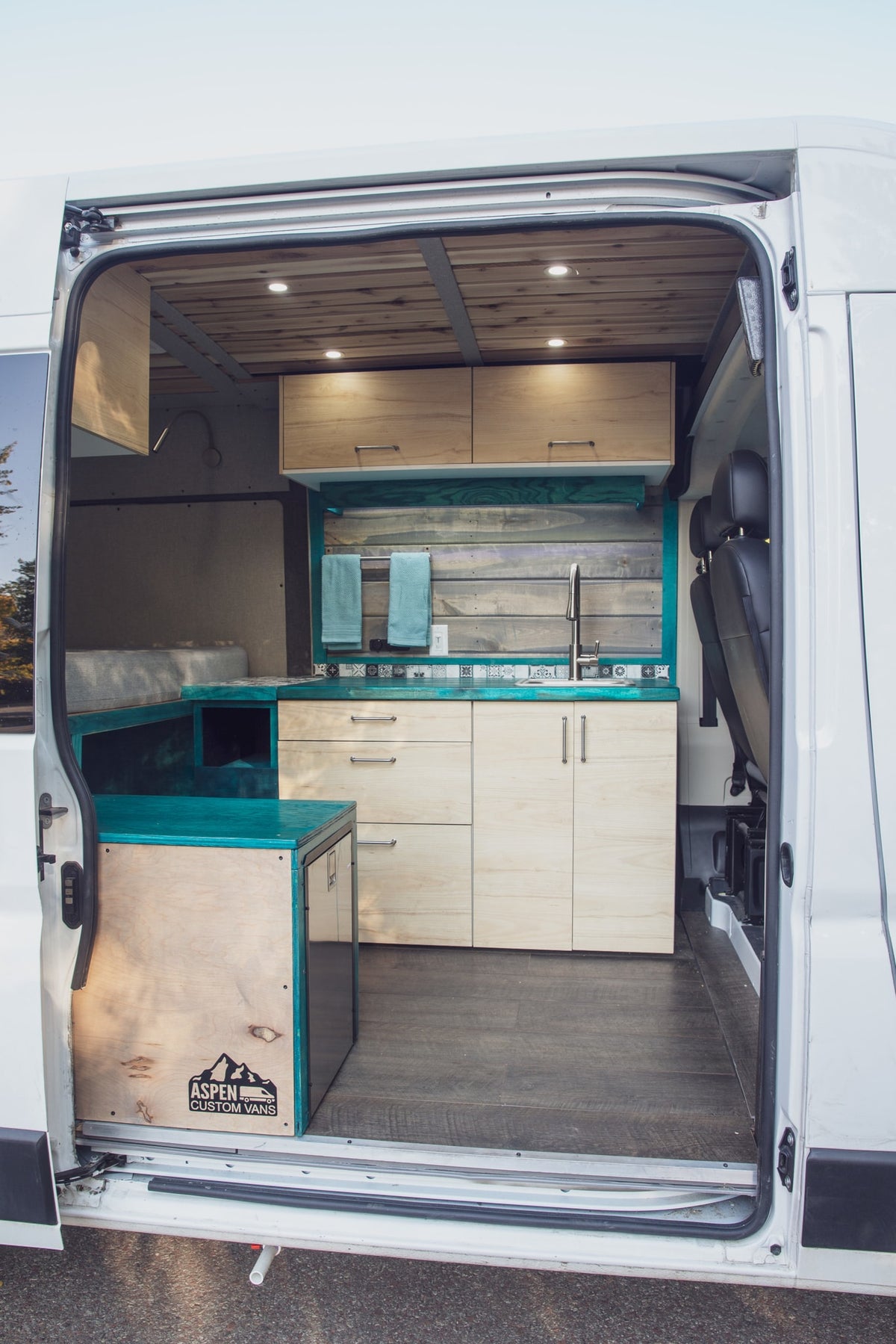 Inside a custom RV rental camper van: modern kitchen, cozy bed, & stylish wood interior accents from Aspen Custom Vans. — photo 2