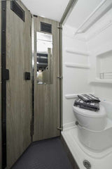 Inside an RV rental: a compact bathroom with white toilet, integrated shower, and wood-look privacy door.