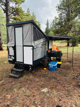 Forest camping adventure with a pop-up RV rental: Viking camper set up with an outdoor kitchen & awning in pine woods.