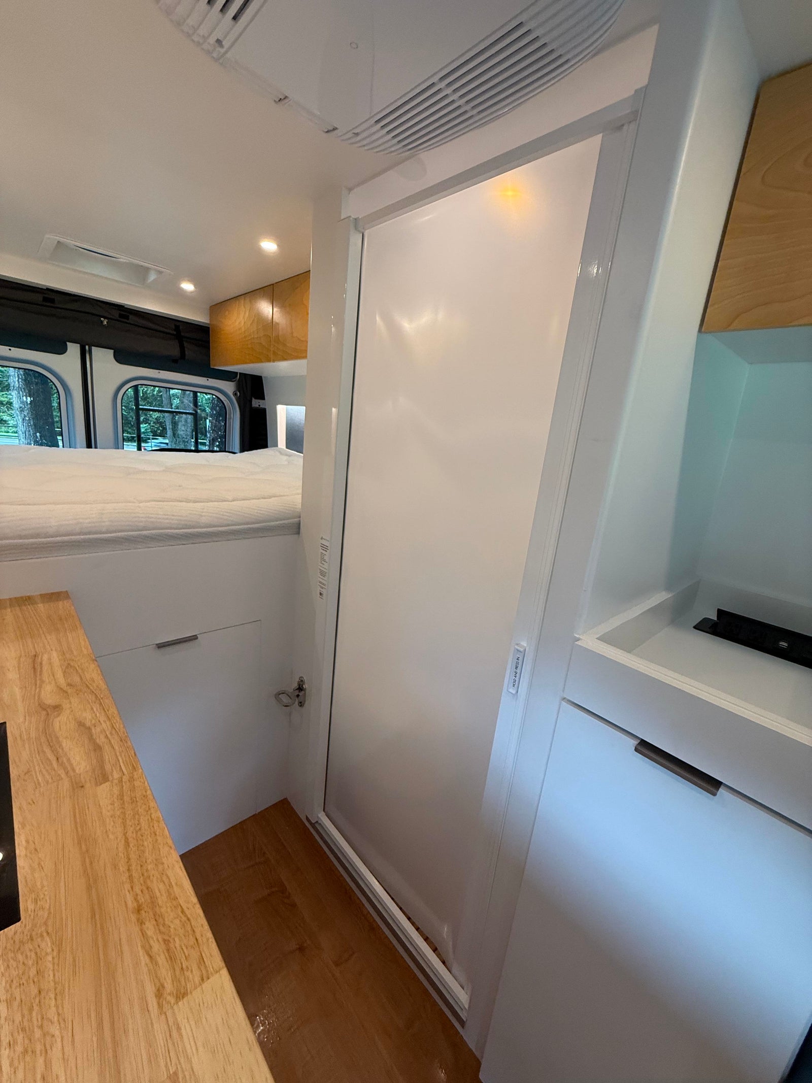 Explore this RV rental's modern interior: raised bed, wood kitchen counter, and sleek white bathroom/shower door.