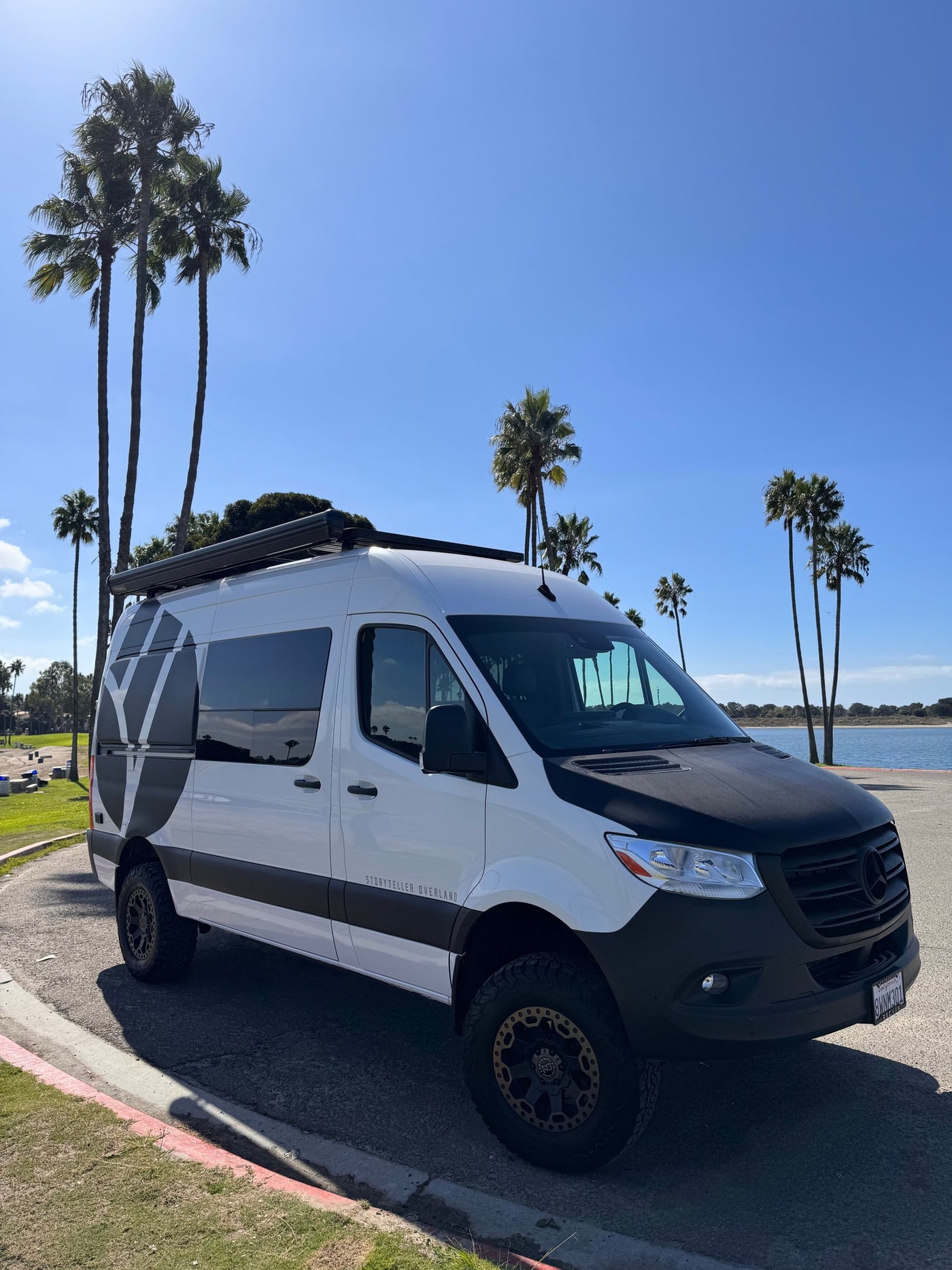 White custom Sprinter camper van for rv rental parked under sunny sky near palm trees and water. Ideal for adventure travel. — photo 19