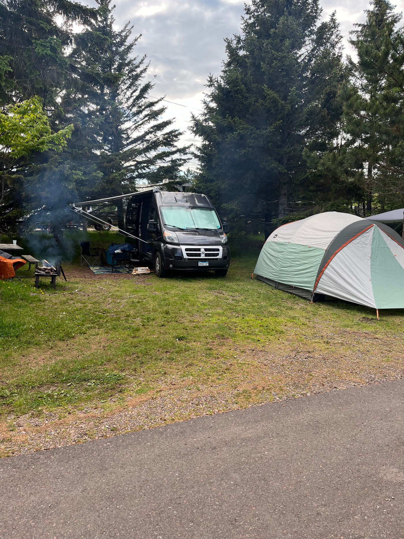Enjoying a serene campsite with an RV rental, a tent, and a warm campfire. Smoke rises among the tall pines. — photo 7