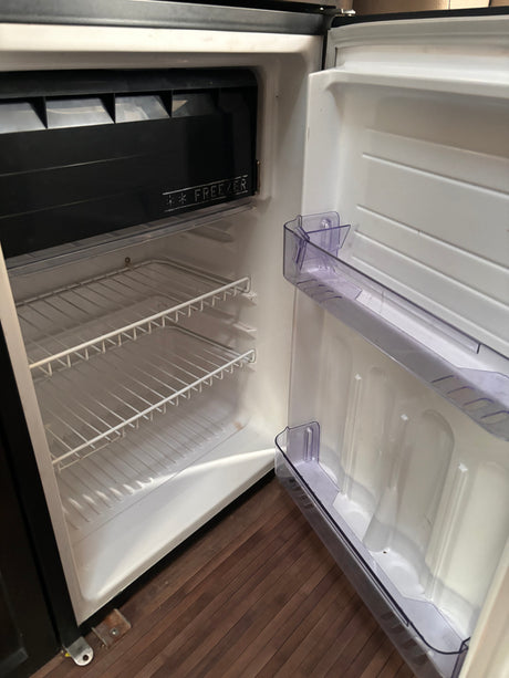 Interior of a compact, empty refrigerator with a freezer compartment and wire shelves, typical for an RV rental.