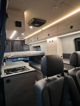Experience comfort in this modern rv rental interior, featuring bright LED lighting, light wood cabinetry, and front seats.