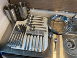 Compact RV rental kitchen features stainless steel cups, plates, and cutlery by the sink.