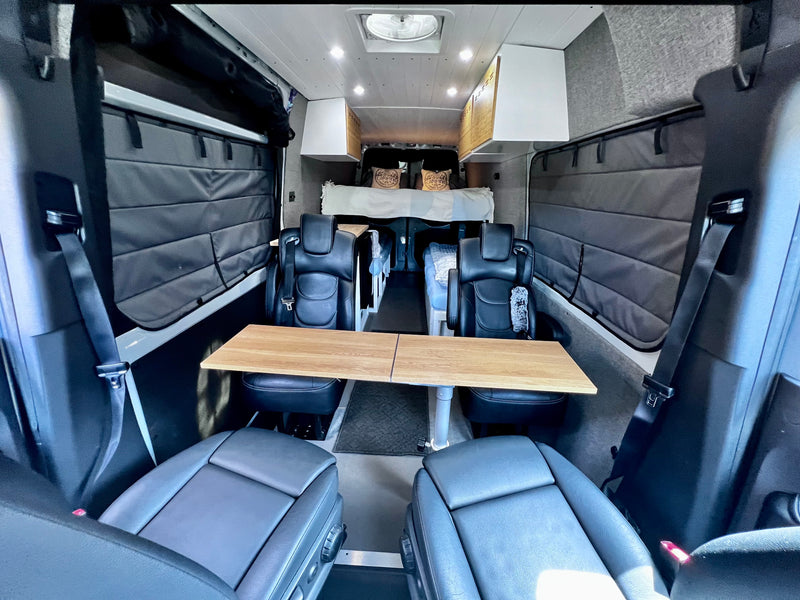 Explore this cozy RV rental interior, featuring swivel chairs, a versatile wooden table, and a comfortable rear bed. — photo 2