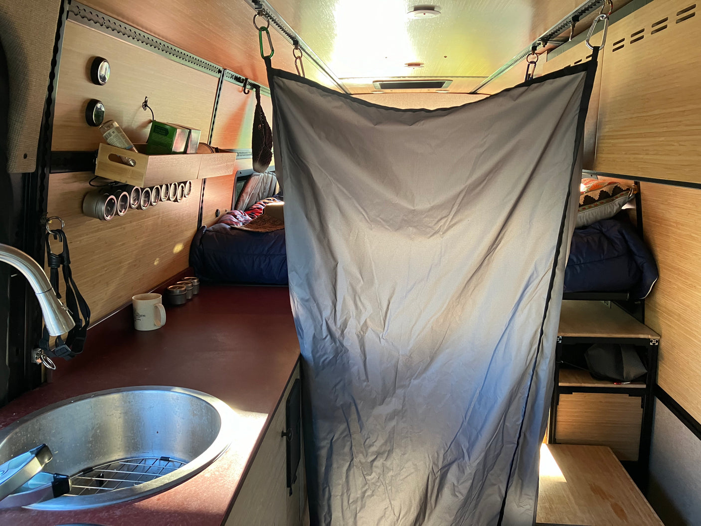 Inside a modern RV rental van: compact kitchen with sink, integrated storage, and a cozy sleeping area separated by a privacy curtain.