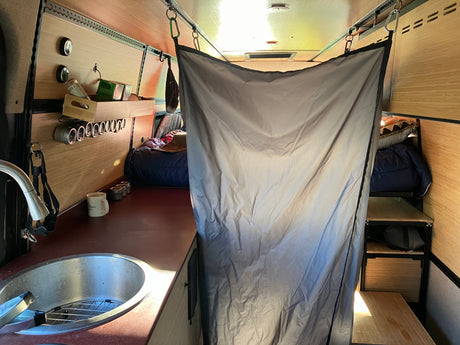 Inside a modern RV rental van: compact kitchen with sink, integrated storage, and a cozy sleeping area separated by a privacy curtain.