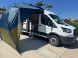 This white RV rental camper van features an attached privacy awning creating an outdoor living space. A step stool is by the open door.
