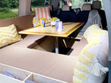 RV rental camper van interior: cozy bench seating, a central table, & decorative pillows.