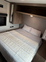 Cozy RV rental bedroom with a striped and quilted bed, overhead storage, and bedside charging, perfect for comfortable journeys.