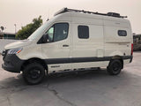 Light-colored Winnebago Revel 4x4 Sprinter van, a popular RV rental for outdoor adventures, parked on asphalt.