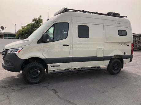 Light-colored Winnebago Revel 4x4 Sprinter van, a popular RV rental for outdoor adventures, parked on asphalt.