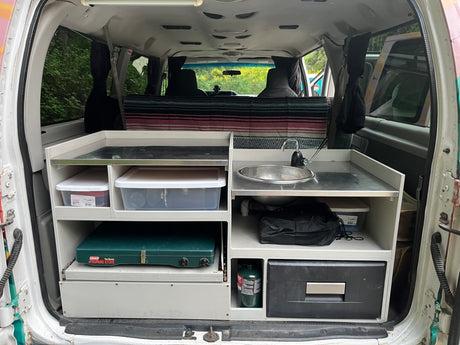 This rv rental features a compact camper van kitchen with a sink, stove, fridge, and storage bins for adventure.