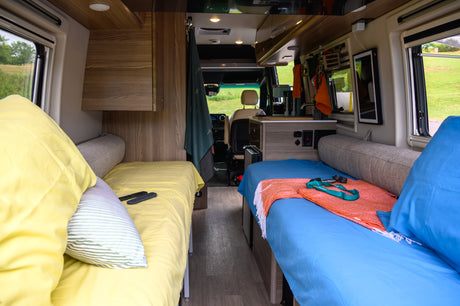 Cozy rv rental interior with twin beds, bright bedding, and compact kitchen. Ideal for a comfortable road trip.