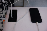 A black smartphone charges via a white cable plugged into a built-in power outlet and USB station on an RV rental surface.