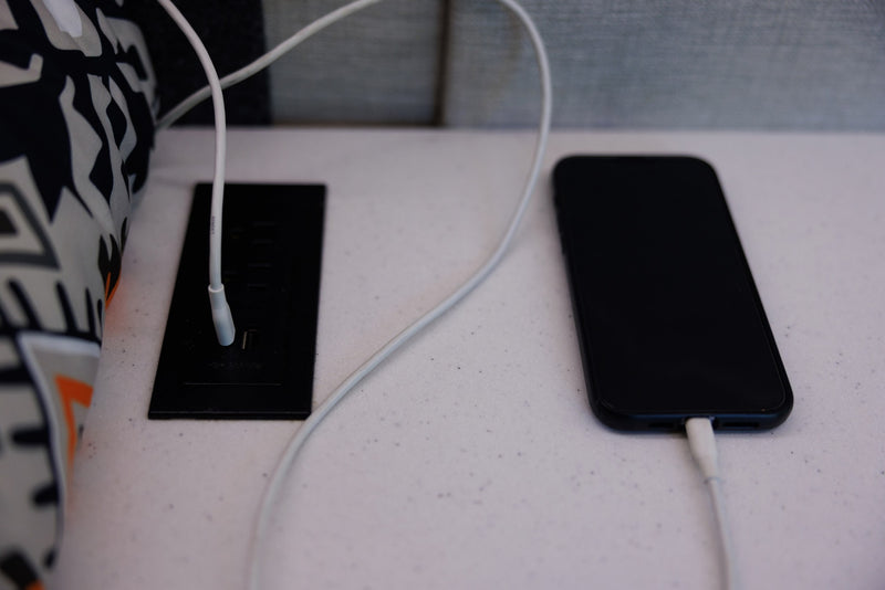 A black smartphone charges via a white cable plugged into a built-in power outlet and USB station on an RV rental surface. — photo 9