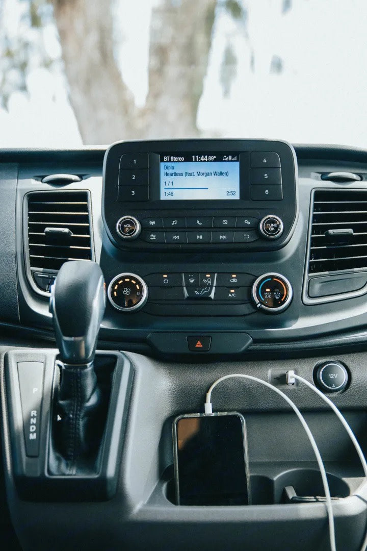 RV rental interior: Dashboard with Diplo's "Heartless" playing on the infotainment system and a phone charging.