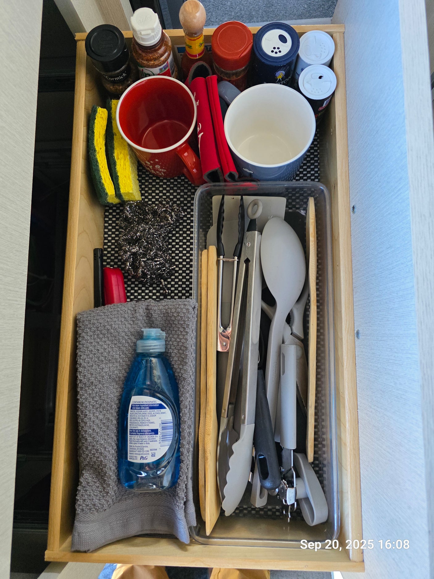 Compact RV rental kitchen drawer featuring essential spices, dish soap, sponges, and cooking tools for travelers.
