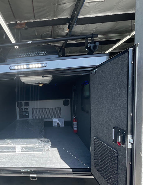 RV rental toy hauler interior: spacious cargo area with ramp door, overhead lighting, control panels, and mattress for versatile use.