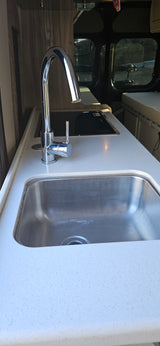 Step inside this RV rental! Features a compact kitchen with a stainless steel sink, chrome faucet, and induction cooktop.