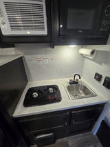 Compact RV rental kitchen featuring a microwave, two-burner stovetop, and sink, designed for efficient use of space.
