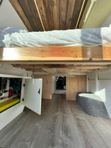 View beneath the raised bed of this RV rental, showcasing organized under-bed storage, electrical systems, and wooden flooring.