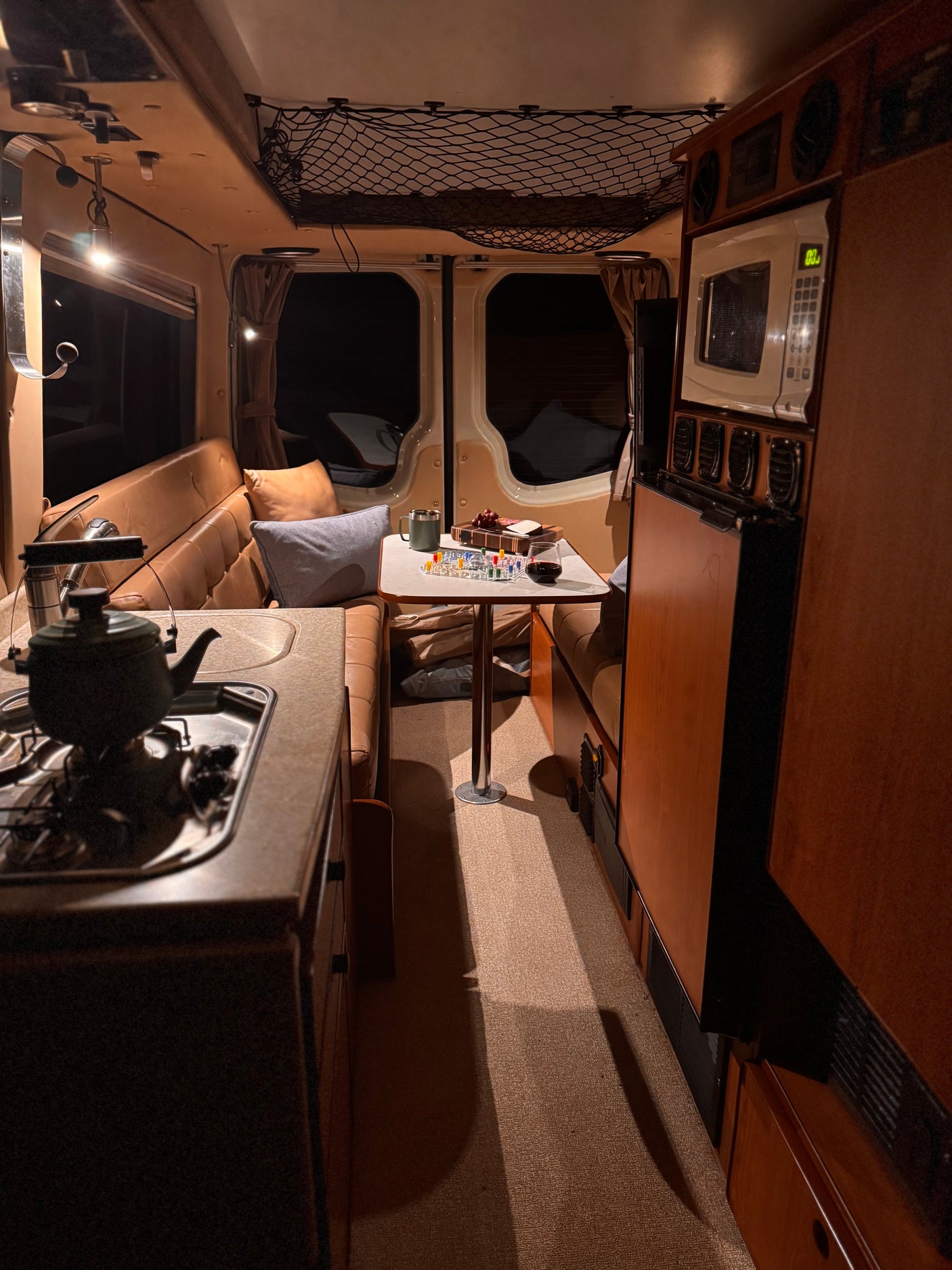 Cozy RV rental interior at night, featuring a dining area with a board game, snacks, and a kitchenette.