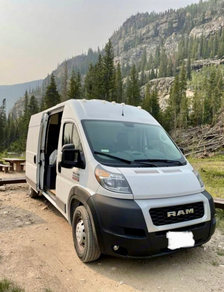 Explore nature with this Ram ProMaster RV rental. White van parked on a dirt road, surrounded by scenic mountains.
