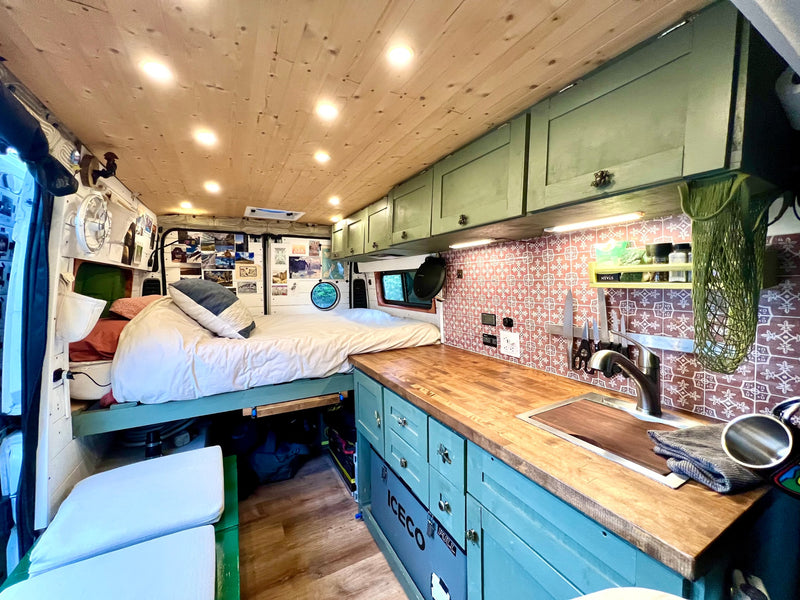 This RV rental boasts a comfortable bed, full kitchen with sink, and custom teal cabinetry, offering cozy travel accommodations. — photo 4