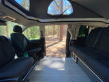 Spacious RV rental interior: pop-top camper with open side door revealing a serene forest campsite view.