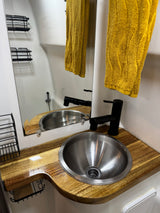 A modern, compact RV rental bathroom with a stainless steel sink, black faucet, and wooden counter. Yellow towels hang beside the mirror.