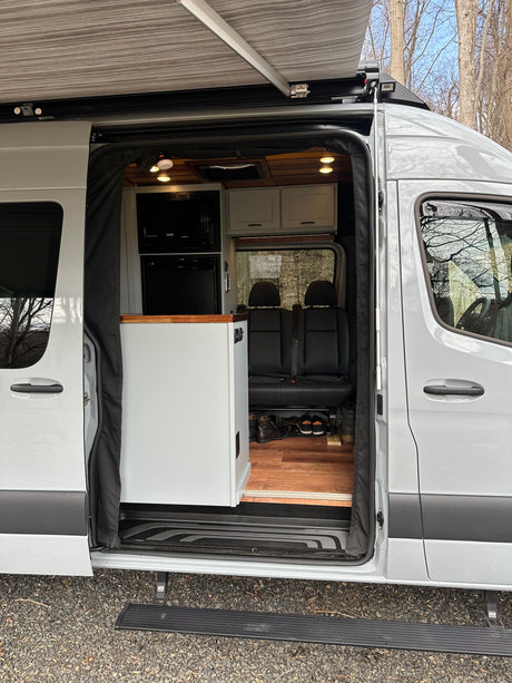 Explore this spacious RV rental camper van with its open side door, showcasing a modern kitchenette, seating, and extended awning.