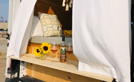 This inviting rv rental offers a cozy retreat: open van with curtains, wine, and sunflowers for relaxing outdoor adventures.