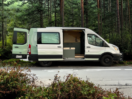 A custom Ford Transit camper van with open doors, revealing its unique interior and exterior design. Perfect for an RV rental adventure in nature.