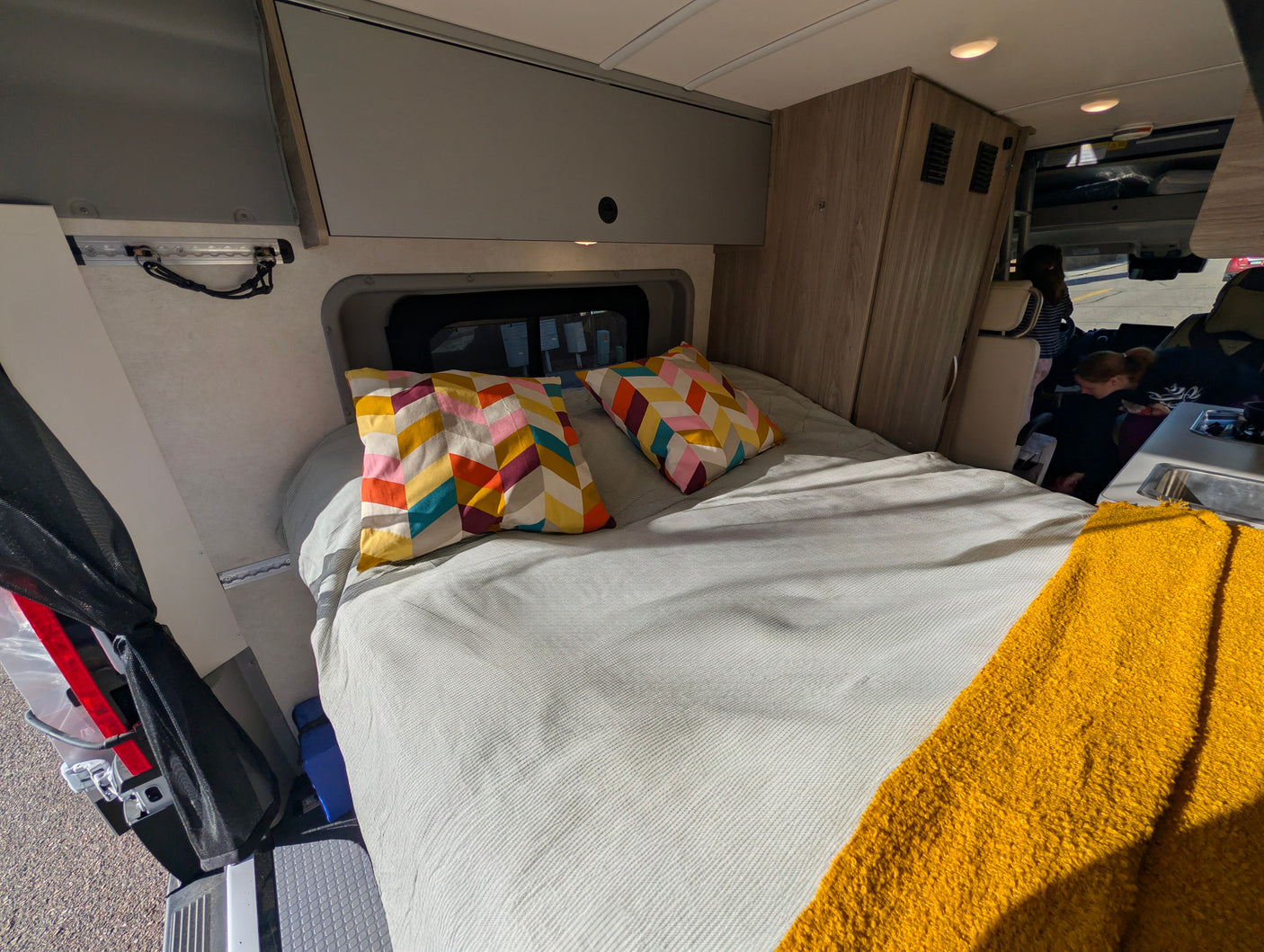 Comfortable rv rental sleeping area with bright pillows, cozy duvet, and overhead cabinets for mobile adventures.