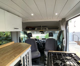 Modern rv rental camper van interior with kitchen, wood ceiling, and driver/passenger seats visible.